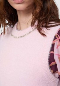 Maglione rosa chiaro, morbido, con scollo arrotondato e dettaglio a catena d'argento. Lo strato interno presenta un motivo floreale in bordeaux e rosa.