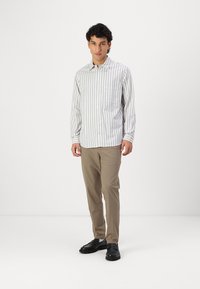 Cămașă cu dungi, de culoare gri deschis și alb, cu mâneci lungi și un buzunar, asortată cu pantaloni bej și pantofi negri.