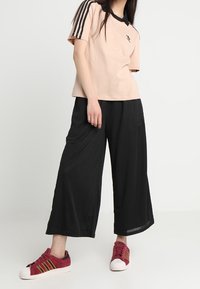 Ljusrosa sportskjorta med svart krage och ränder, kombinerad med svarta vida byxor och röda sneakers med gula ränder.