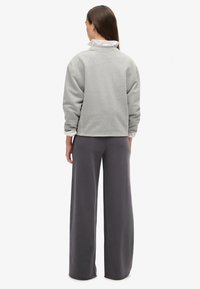 Lichtgrijze sweatshirt met elastische boorden, gecombineerd met donkergrijze wijde broek. De outfit heeft een gelaagd uiterlijk met een witte kraag eronder.
