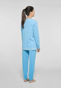 Set di pigiama azzurro chiaro composto da una maglietta a maniche lunghe con motivo floreale e bordi in pizzo, abbinata a pantaloni tapered coordinati. Tessuto morbido.