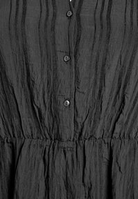 Musta mekko, jossa on pystysuora tekstuuri, napit ja laskostettu vyötärö. Valmistettu kevyestä kankaasta, jossa on huomaamatonta laskostusta.