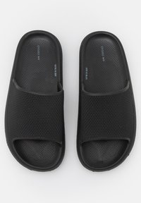 Black slide sandals with a textured mesh design, open toe, and flat sole. Features a smooth, flexible upper material for comfort.