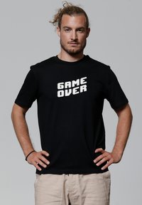 Schwarzes T-Shirt mit weißem pixeliertem Text, der "GAME OVER" sagt. Kurze Ärmel und Rundhalsausschnitt, aus Baumwollstoff gefertigt.