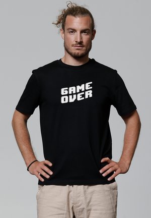 Zwarte T-shirt met witte pixelachtige tekst die "GAME OVER" zegt. Korte mouwen en een ronde halsvorm, gemaakt van katoen.
