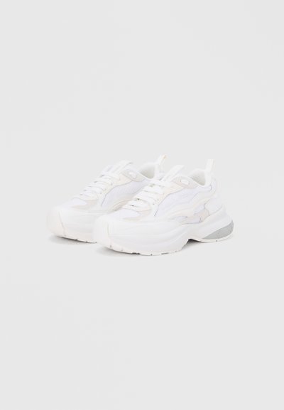 Ζευγάρι λευκά αθλητικά παπούτσια με λεπτομέρειες από δίχτυ και δέρμα, κορδόνια και παχιά λαστιχένια σόλα πάνω σε απλό φωτεινό φόντο.