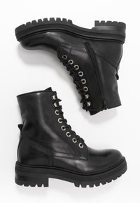 Bottines en cuir noir avec une semelle en caoutchouc noir robuste, fermeture à lacets avec œillets métalliques et fermeture éclair latérale pour un enfilage facile.