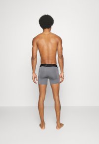 Calzoncillos cortos grises con una cinturilla negra, que presentan un ajuste ceñido y una textura suave, exhibidos en un modelo masculino con la piel desnuda visto desde atrás.