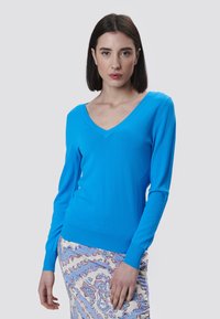 Blauer V-Ausschnitt-Pullover aus weichem Strickstoff mit langen Ärmeln und gerippten Bündchen, kombiniert mit einem gemusterten Rock.