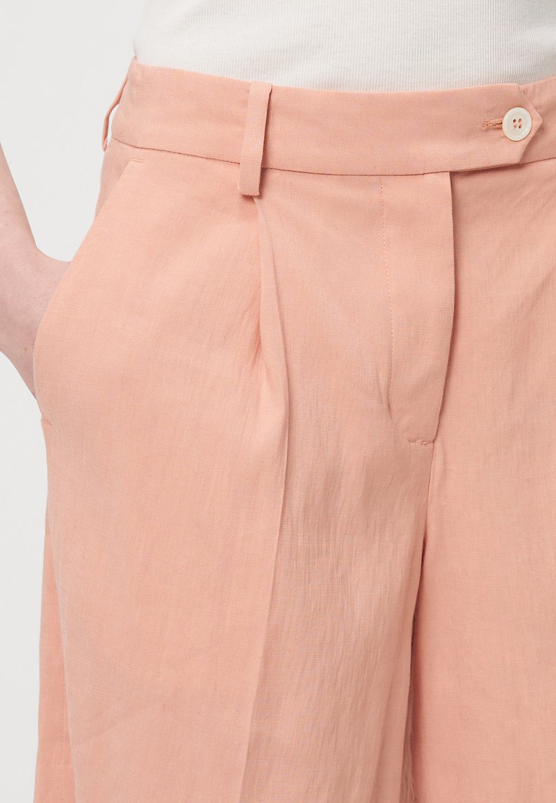 Pfirsichfarbene Leinenhosen mit eingelegtem Vorderteil, einem Knopfverschluss und Seitentaschen. Glatte Textur, maßgeschneiderter Schnitt.