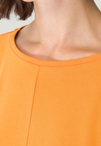 Oranges Oberteil mit rundem Ausschnitt, strukturiertem Stoff und einer mittigen Nahtdetail für zusätzliche Form.