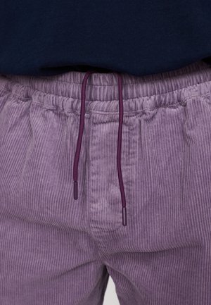 Paarse corduroy broek met verticale geribbelde textuur en een elastische tailleband. Voorzien van een paarse trekkoord met puntige uiteinden voor aanpassing.