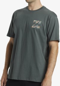 Camiseta de algodón de color gris oscuro con mangas cortas y cuello redondo. La parte frontal presenta un diseño gráfico multicolor de formas abstractas.