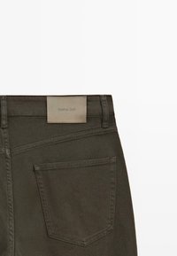 Donkergroene denimbroek met zicht op de achterzak en een beige rechthoekig label met de tekst "Massimo Dutti".