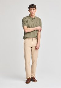 Grön polo t-shirt med korta ärmar och en liten broderad logga, i kombination med beige byxor och bruna snörskor.