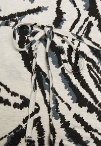 Tecido de algodão com um padrão abstrato texturizado em preto e azul sobre um fundo bege claro, apresentando um detalhe amarrado na cintura.