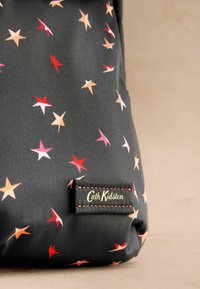 Zwarte stoffen tas met een meerkleurige sterrenprint in rood, roze en oranje. Voorzien van een merkpatch met rode stiksels.
