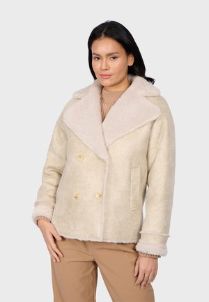 Giacca beige doppiopetto con un grande colletto e polsini morbidi di un beige chiaro. Presenta una tasca frontale e un tessuto liscio e strutturato.