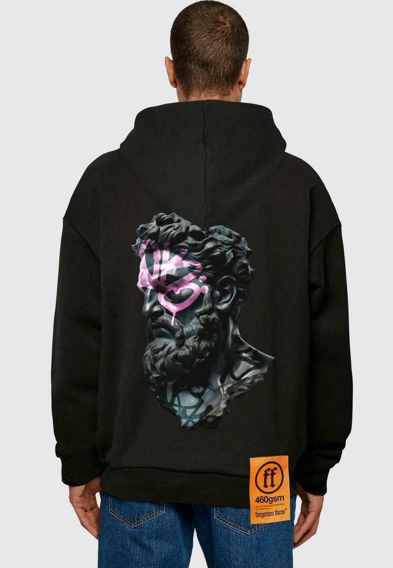 Homme portant un sweat à capuche noir avec un buste imprimé d'une statue barbu recouvert de graffiti roses et noirs dans le dos et une étiquette orange près de l'ourlet.