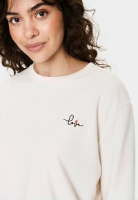 Sweatshirt rose clair à col rond, avec une broderie en écriture noire du mot 'love' accompagnée d'un petit cœur rouge.