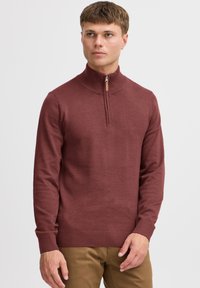Sweat-shirt zippé bordeaux avec col et poignets côtelés, fabriqué en tissu tricoté doux. Présente une courte fermeture éclair et une finition texturée.