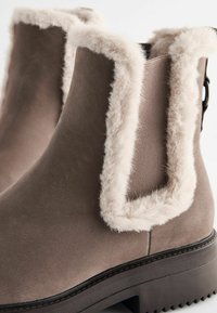 Bruine enkelboots met een zachte, nepbont kraag en een gestructureerd buitenmateriaal. Heeft een stevige zool en een slanke silhoeet.