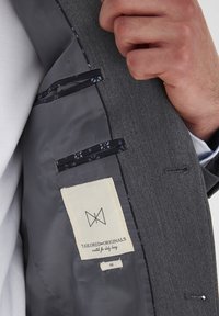 Harmaa takki, jossa on sileä tumma vuori, kaksi mustalla trimmitaskua ja vaalean beige etiketti, jossa lukee "TAILORED ORIGINALS", koko 48.