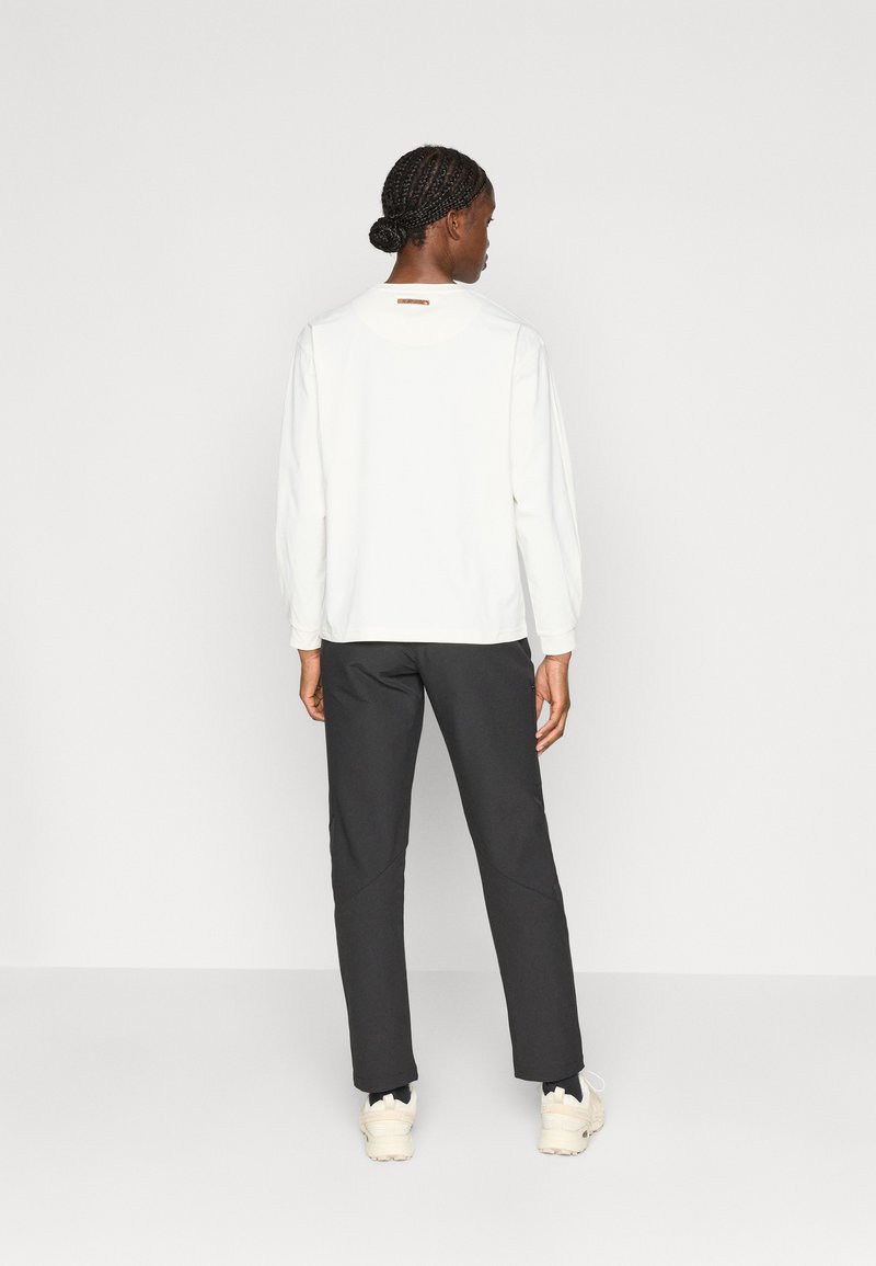 Haut à manches longues blanc avec un col rond et un tissu texturé, associé à un pantalon gris foncé fuselé. Les détails notables incluent un petit logo sur le dos.