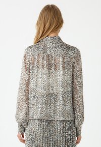 Transparante blous met luipaardprint, lange mouwen, geplooid achterdetail en knoop manchet. Zachte textuur in beige, zwart en bruin tinten.