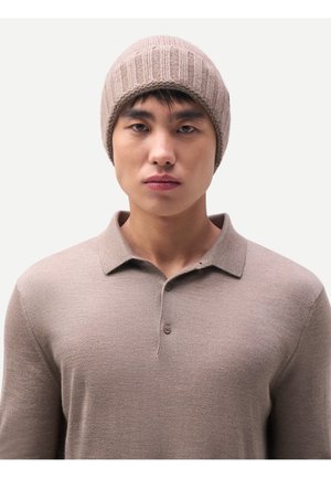 Young man wearing a beige knit beanie and matching beige long-sleeve polo shirt, facing forward with neutral expression.