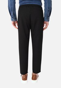 Pantaloni neri a vita elasticizzata con taglio dritto, caratterizzati da spacchi laterali all'orlo. Indossati con scarpe in pelle marrone e una camicia di jeans blu.