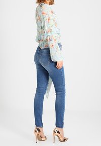 Světle modrá květinová blůza s volánovými rukávy, doplněná tmavě modrými skinny džíny a metalickými růžově zlatými vysokými podpatky.