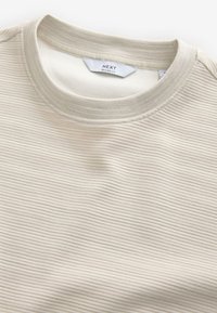 Ljusbeige ribbad sweatshirt med rund hals gjord av texturerat tyg, med en avslappnad passform och en etikett med texten "NEXT."