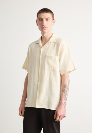 Short-sleeve, light yellow shirt made of textured fabric with a chest pocket, button closure, and a relaxed fit.