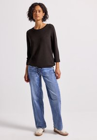 Czarny sweter z okrągłym dekoltem i rękawami 3/4 w połączeniu z jasnoniebieskimi, szerokimi dżinsami z kieszenią ściąganą w pasie oraz białymi trampkami.