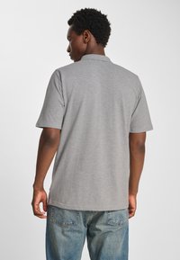 Szara koszulka polo z kołnierzykiem, krótkimi rękawami i luźnym krojem. Tkanina wydaje się gładka z delikatną teksturą. Noszona z wyblakłymi niebieskimi dżinsami.