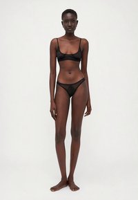 Zwarte kant bralette met dunne bandjes en geschulpte randen, gecombineerd met een bijpassende string met bloemensieraden en transparante panelen.