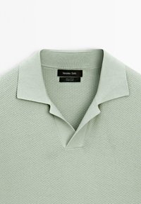 Polo shirt in cotone verde chiaro con un motivo testurizzato, dotato di colletto classico e scollatura a V. Etichetta visibile all'altezza del collo.