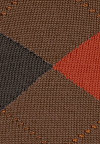 Primo piano di un tessuto lavorato a maglia con un motivo a diamante marrone, grigio scuro e arancione, con piccoli accenti di punto arancione.