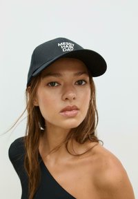 Schwarze Baseballkappe mit weißem Text "MESSY HAIR DAY", gebogener Schirm und glattes Gewebe. Das Modell hat langes, welliges Haar, das teilweise sichtbar ist.