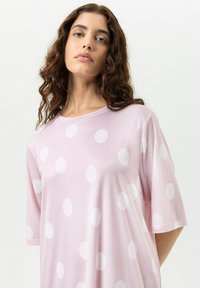 T-shirt rose à manches courtes en tissu doux avec de grands pois blancs. Le modèle présente une coupe décontractée et un col rond.