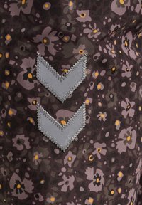 Blommönstrad textil med en mörk lila bas, som har grå zigzag-sticksömmar och små gula detaljer här och där.