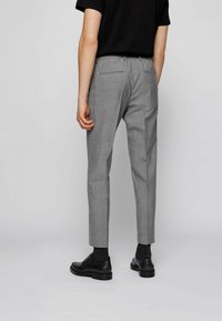 Grå skräddarsydda byxor med smal passform, slät textur, elastiskt midjeband och två bakfickor. Matchas med svarta skor och strumpor.