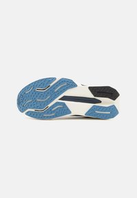 Suola della scarpa con scanalature per la trazione, prevalentemente blu con accenti bianchi e neri. Materiale resistente con superficie testurizzata e design simmetrico.