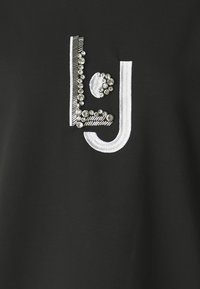 Zwarte stof met een decoratief ontwerp van zilveren draad en heldere strasstenen, die letters en patronen vormen. Glad textuur.