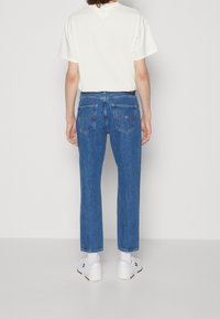 Blå denimjeans med rak modell, femficksdesign och subtila sömmar, kombinerade med en vit t-shirt och vita sneakers.