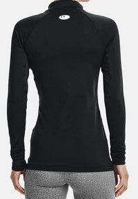 Musta pitkähihainen urheilupaita, jossa on korkea kaula-aukko ja vartalonmyötäinen muotoilu. Takana on pieni logo ja kangas on sileä ja joustava.