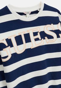 Marineblauw-wit gestreept T-shirt met een ronde hals en een geborduurd "GUESS" logo in perzikkleur op de voorkant. Gemaakt van katoen, casual ontwerp.