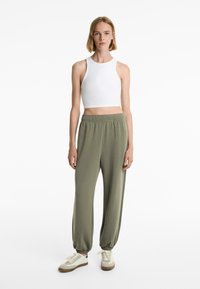 Let og hvidt ribbet crop top og løstsiddende olivenfarvede sweatpants med elastiske manchetter, parret med beige og hvide træningssko.