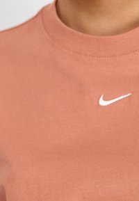 Helles rosa Baumwoll-Sweatshirt mit Rundhalsausschnitt und geripptem Kragen, mit kleinem weißem Nike-Logo auf der Brust. Glatte Textur.